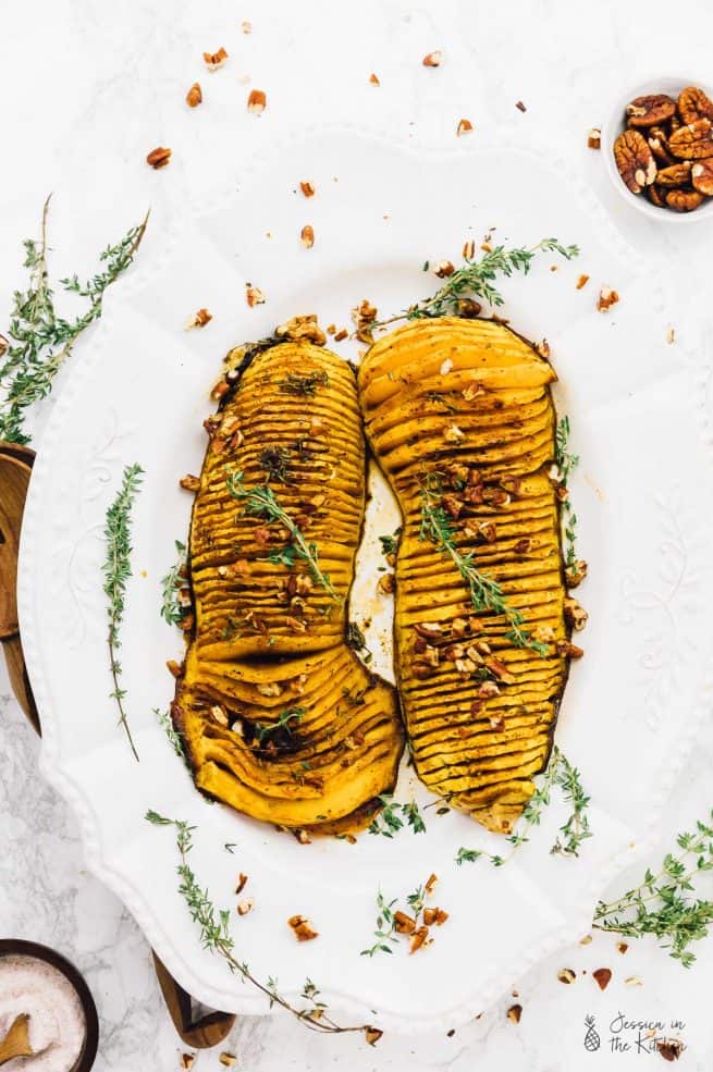 Overhead shot of hasselback butternut squash on a plate, topped with pecans.