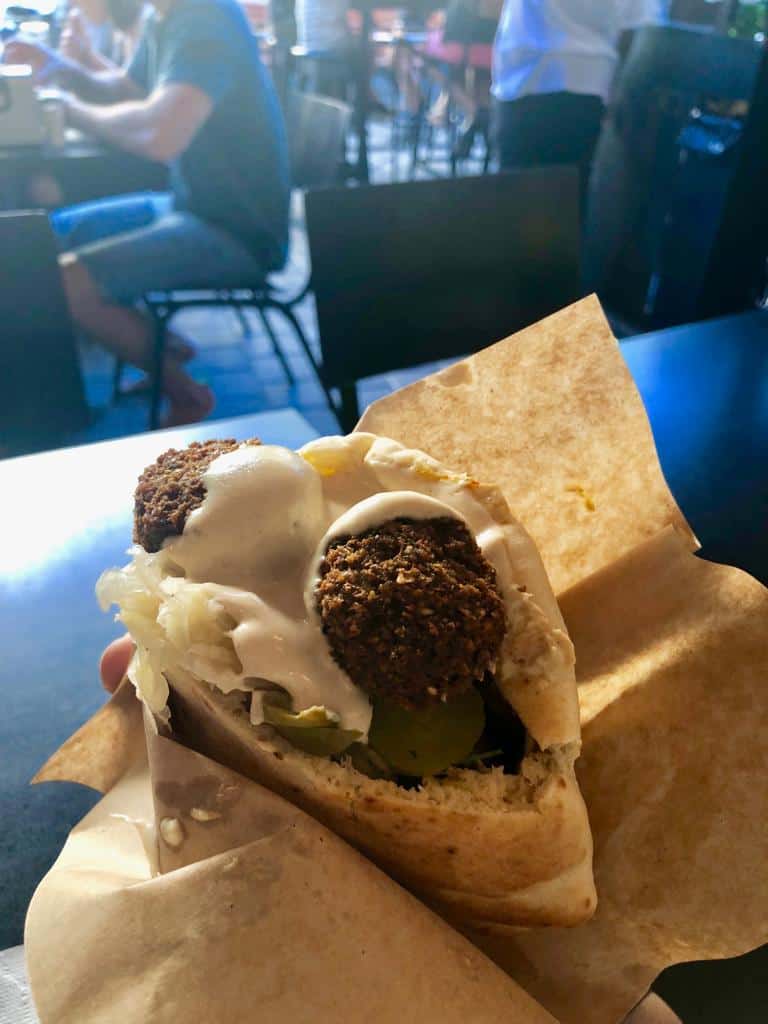Hand holding a falafel in a pita, topped with creamy sauce. 