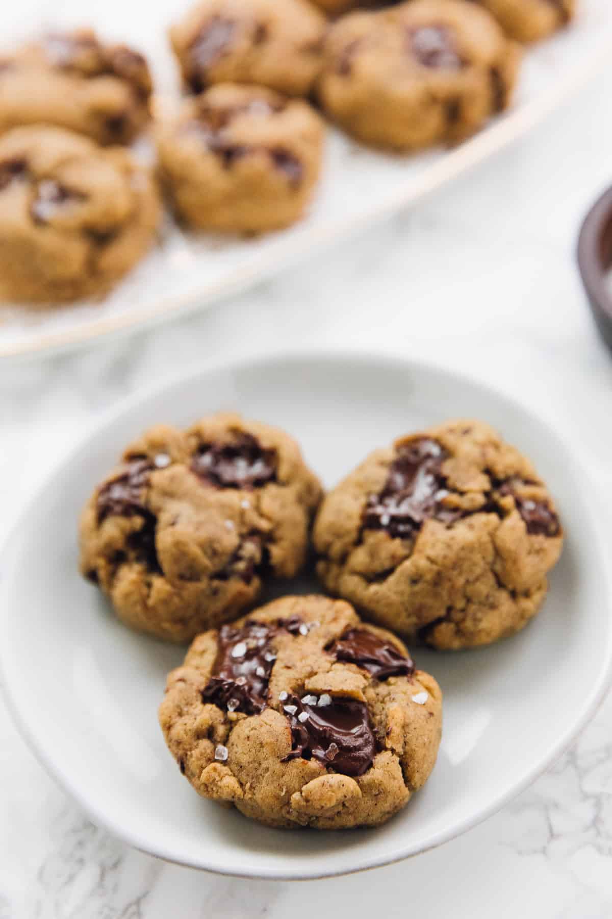 3 Salted chocolate chip tahini cookies on a plate with other cookies in the background