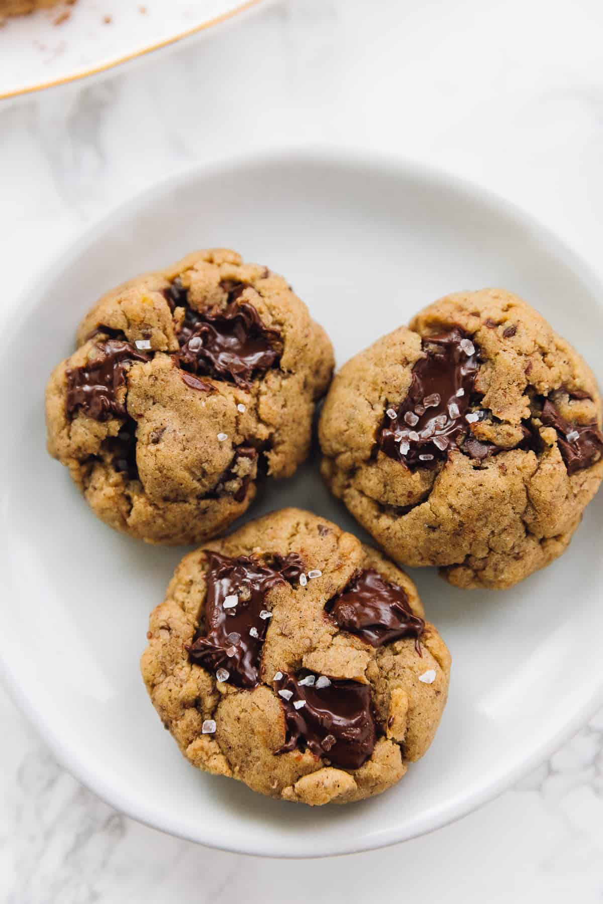 Three salted chocolate chip tahini cookies on a white plate. 