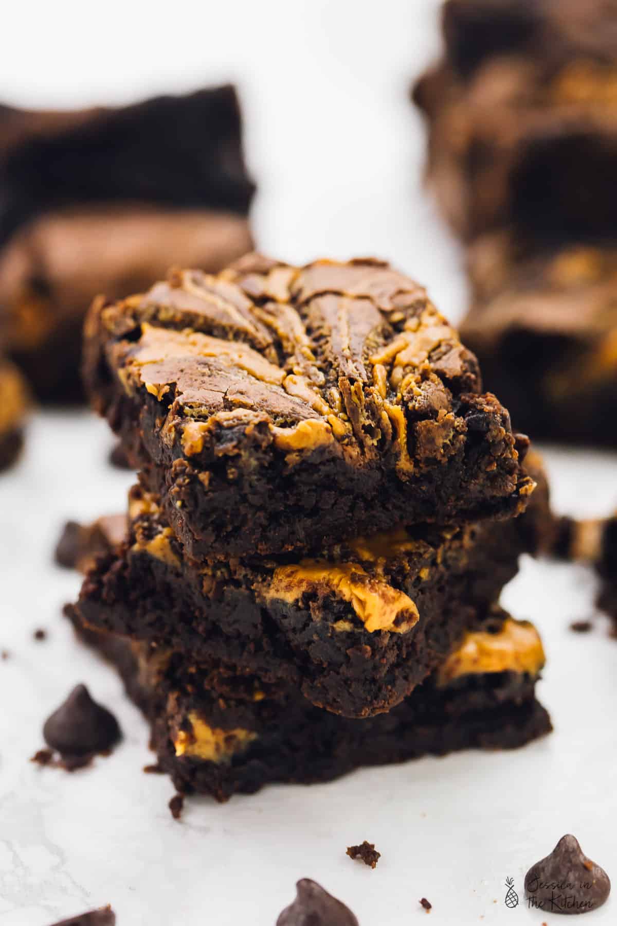 A stack of vegan chocolate peanut butter swirl brownies, surrounded by chocolate chips. 