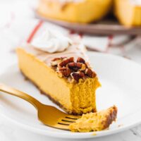 A slice of pumpkin cheesecake on a plate with a piece on a fork.