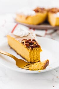 A slice of pumpkin cheesecake on a plate with a piece on a fork.