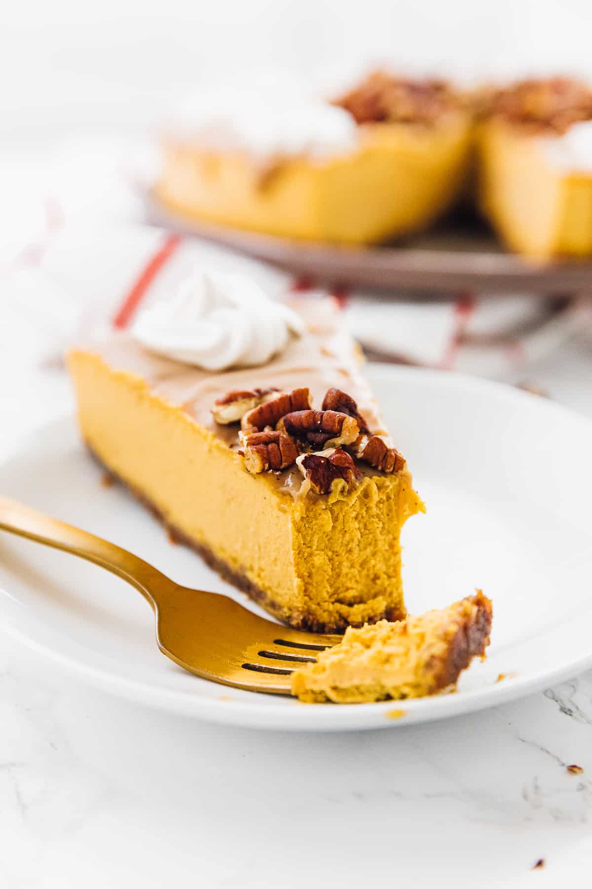 A slice of pumpkin cheesecake topped with nuts and cream cheese, with a fork taking a bite