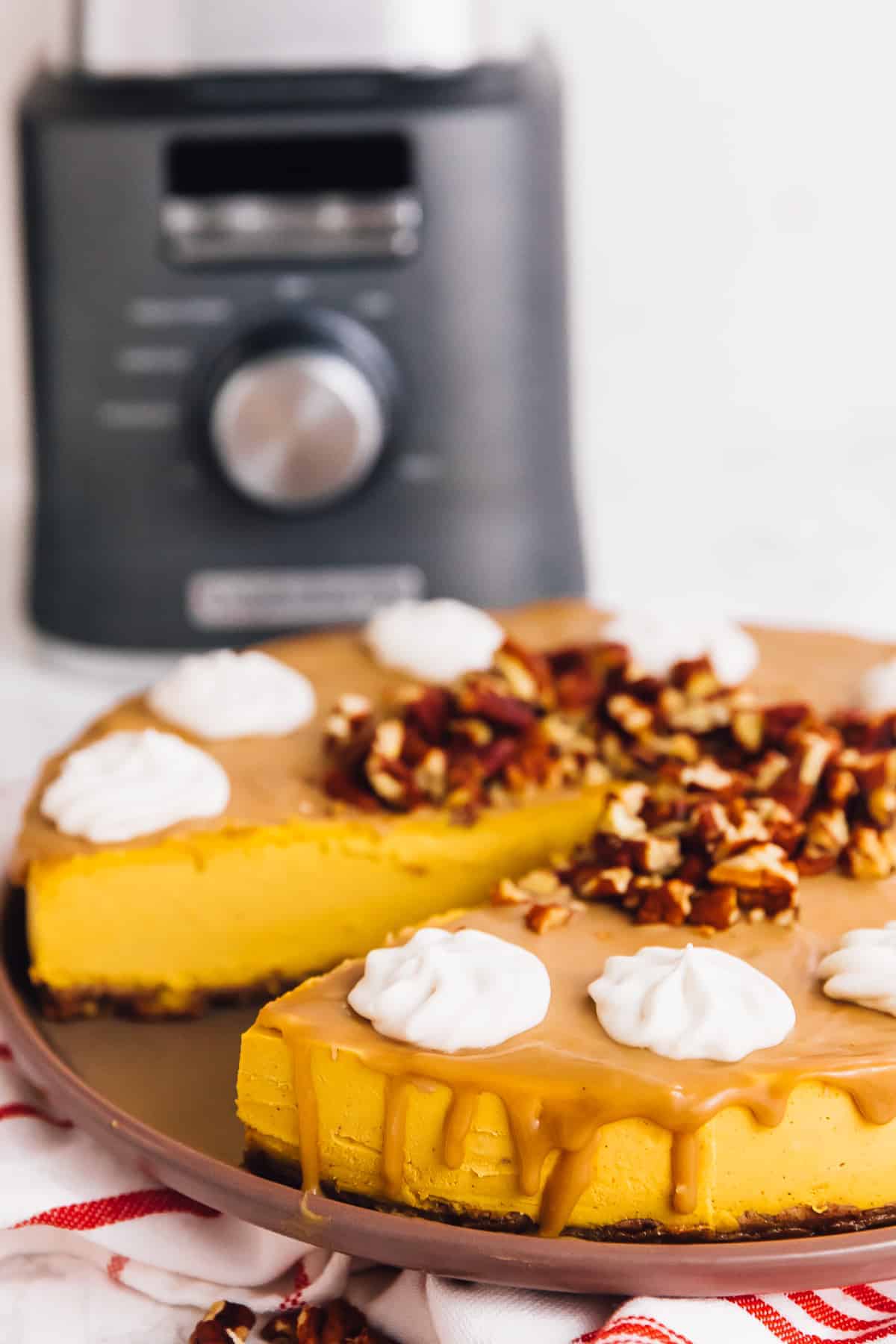 A pumpkin cheesecake topped with nuts, whipped cream, and caramel, with a slice removed