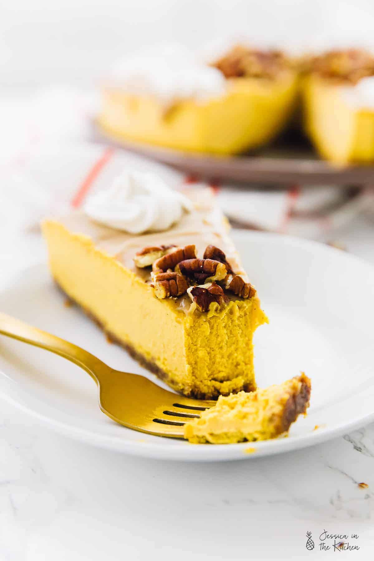 A slice ov vegan pumpkin cheesecake on a plate with a fork. 