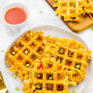 Mac and cheese waffles on a white plate, with sauce on the side.