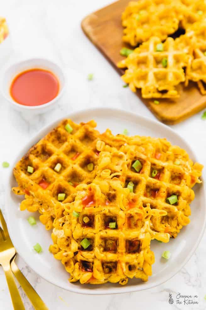 Mac and cheese waffles on a white plate, with sauce on the side.