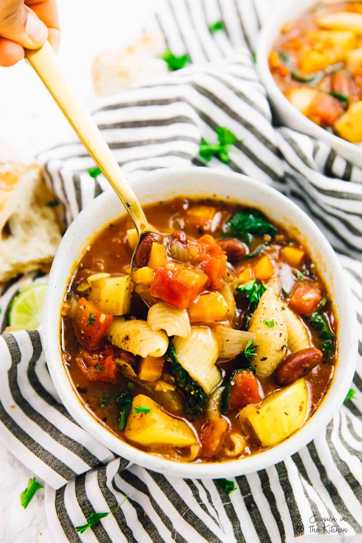 A spoon scooping out some minestrone soup from a bowl. 