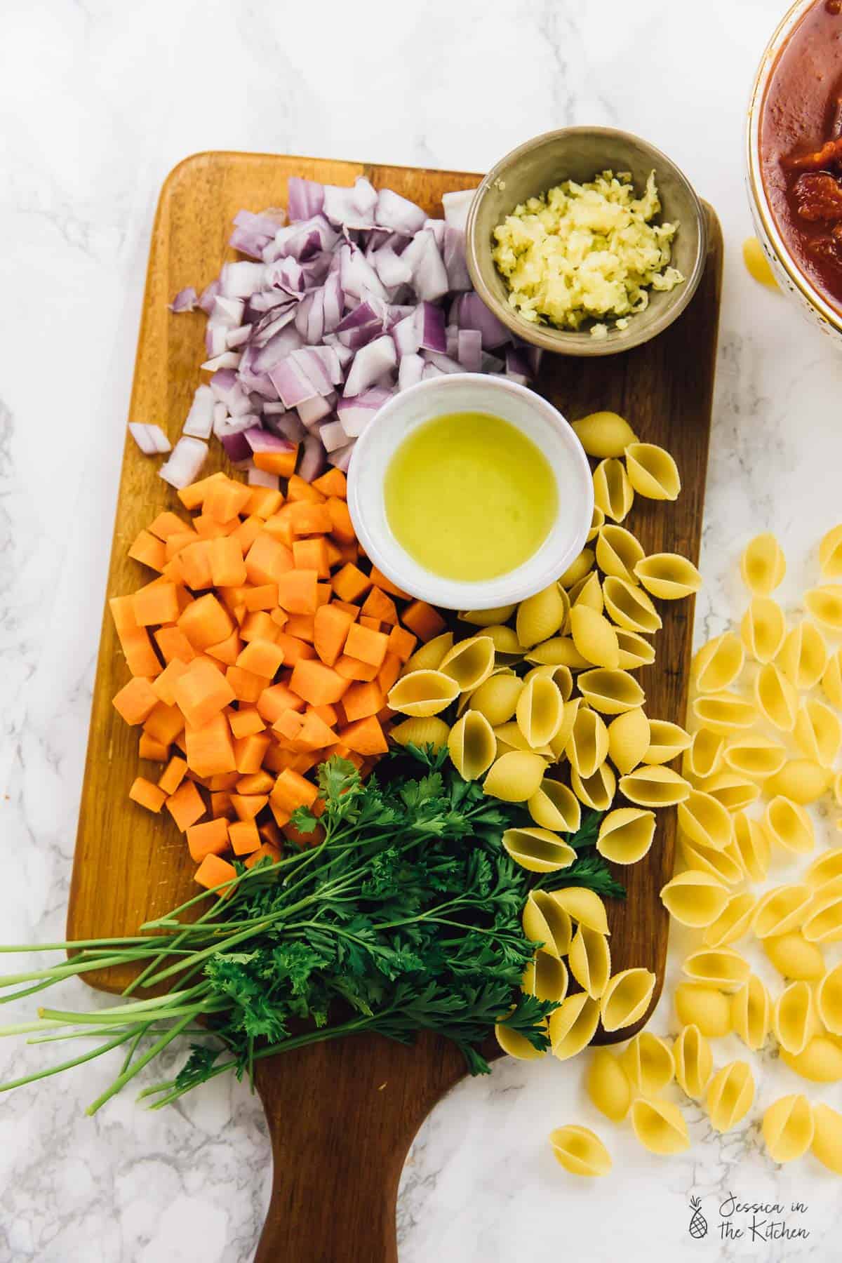 Top down view of cubed sweet potatoes, pasta shells, diced onions, herbs and minced garlic. 