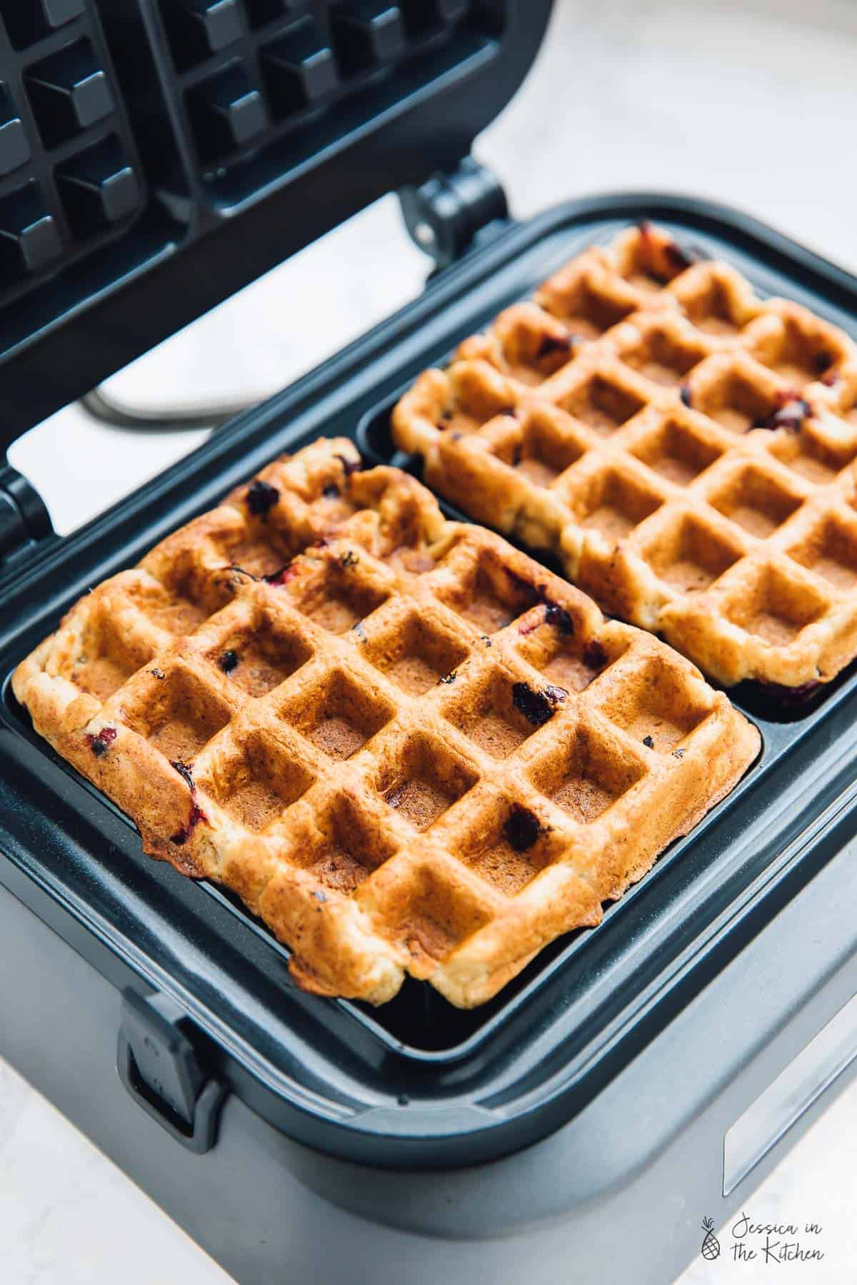 Orange cranberry waffles in an open waffle maker. 