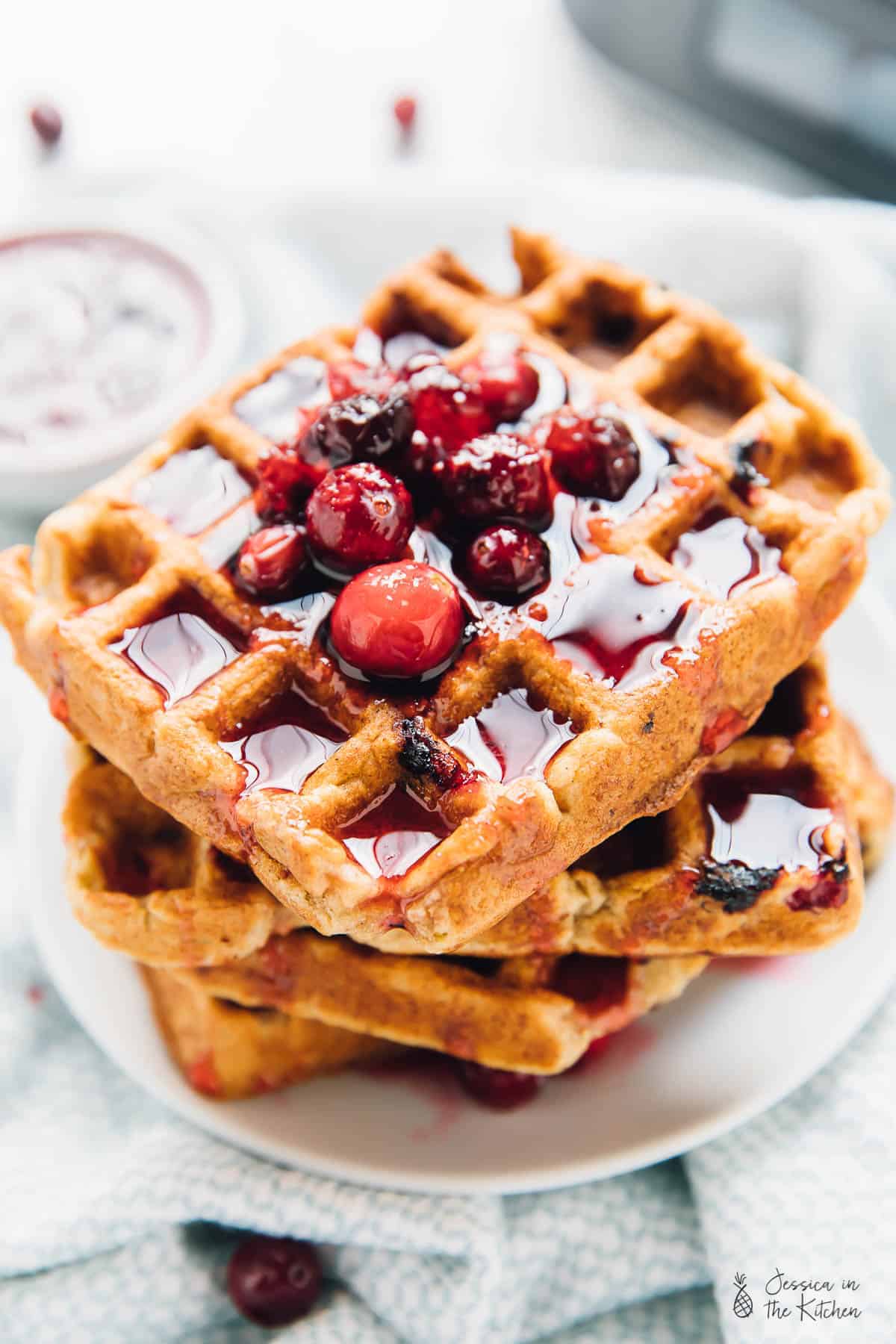 A stack of four orange cranberry waffles, covered in syrup. 