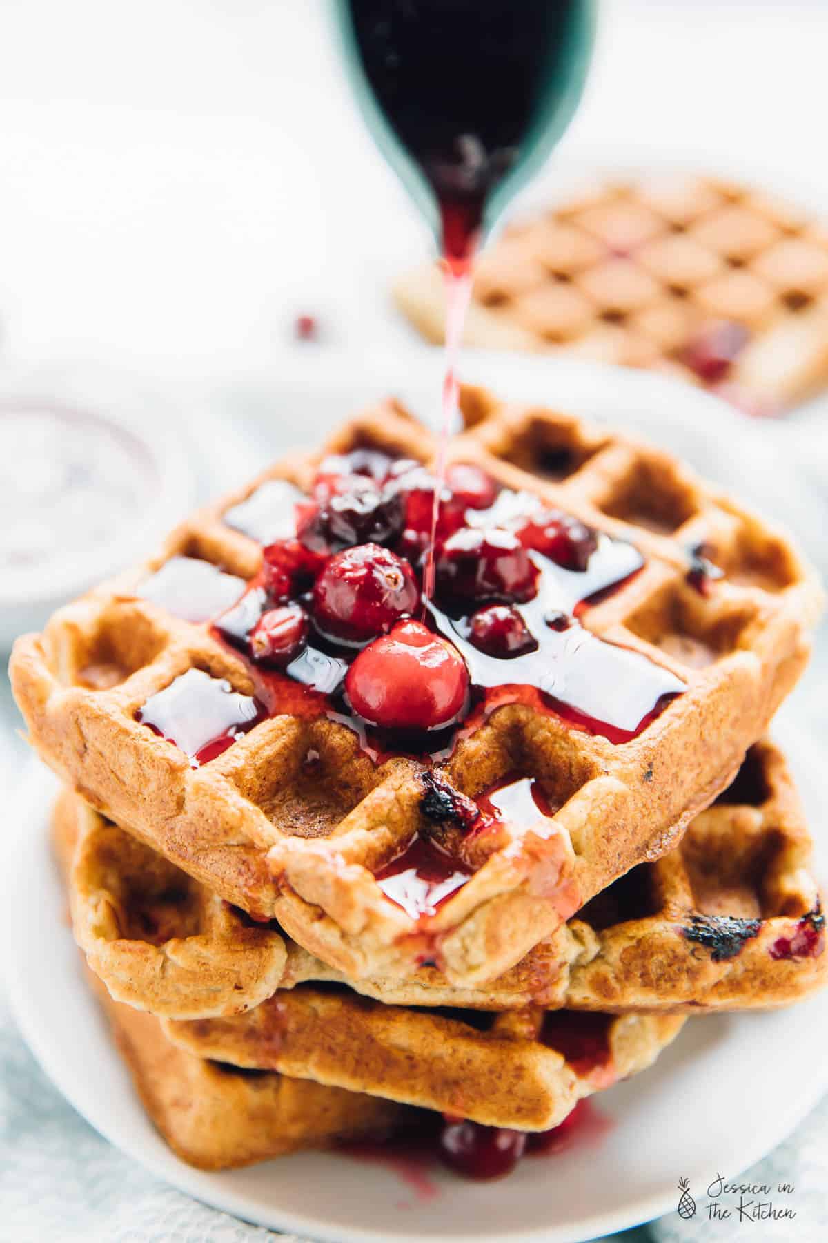 Syrup being poured onto a stack of orange cranberry waffles.