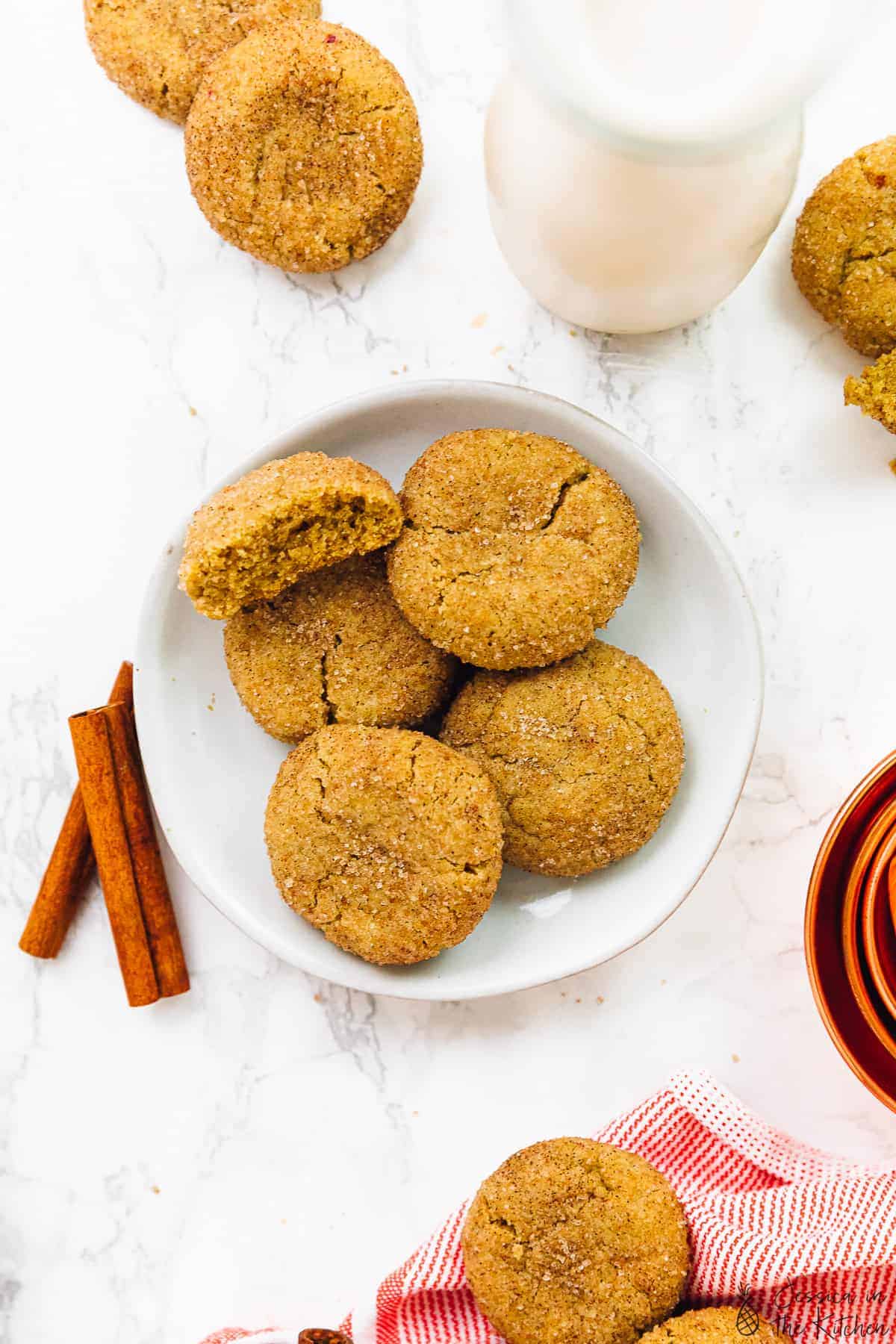 Five snickerdoodle cookies on a plate spread out with cinnamon sticks on the side. 