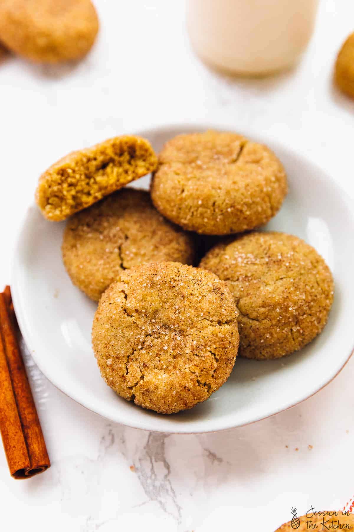 Close up of five snickerdoodle cookies on a plate spread out with cinnamon sticks beside it.