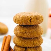 Four snickerdoodle cookies in a stack of four on a plate with cinnamon sticks.