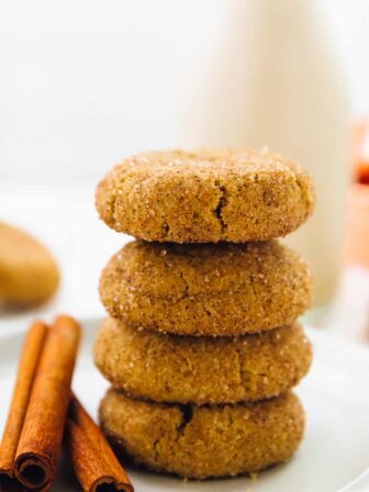 Four snickerdoodle cookies in a stack of four on a plate with cinnamon sticks.