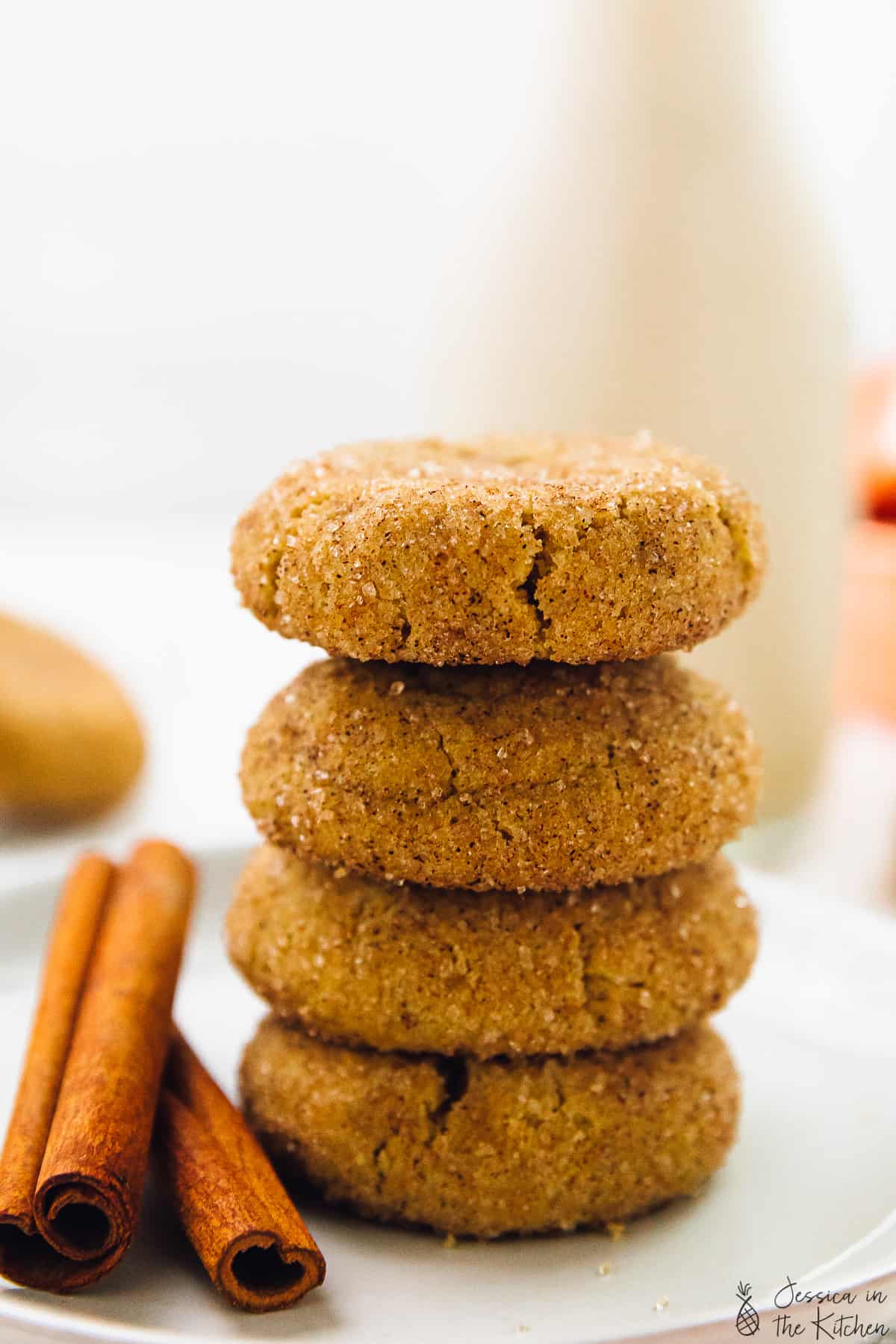 Snickerdoodle cookies in a stack of four on a plate with cinnamon sticks.