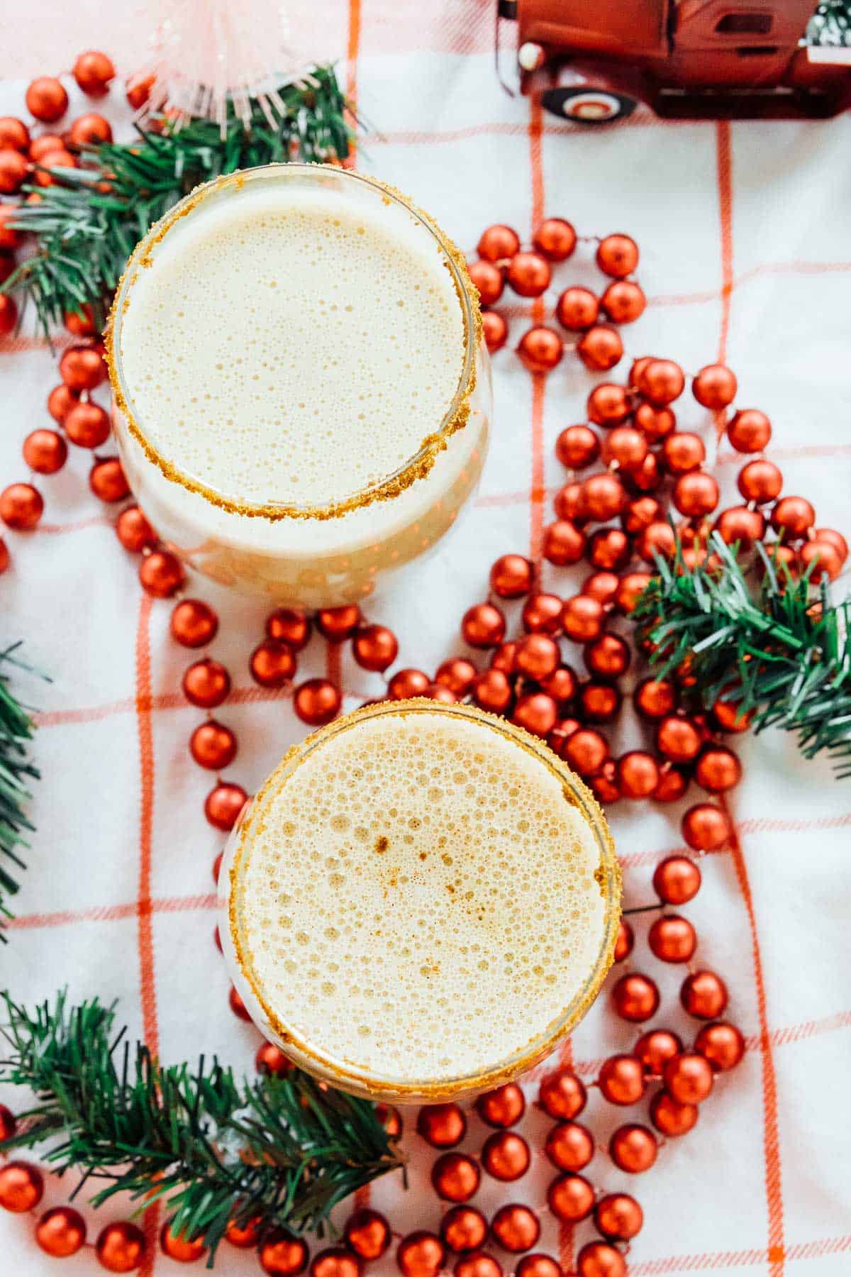 Top down view of vegan eggnog in two glasses, surrounded by holiday decorations. 