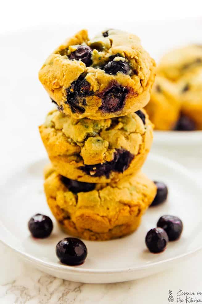 Blueberry muffins stacked on a plate, with loose blueberries on the side.