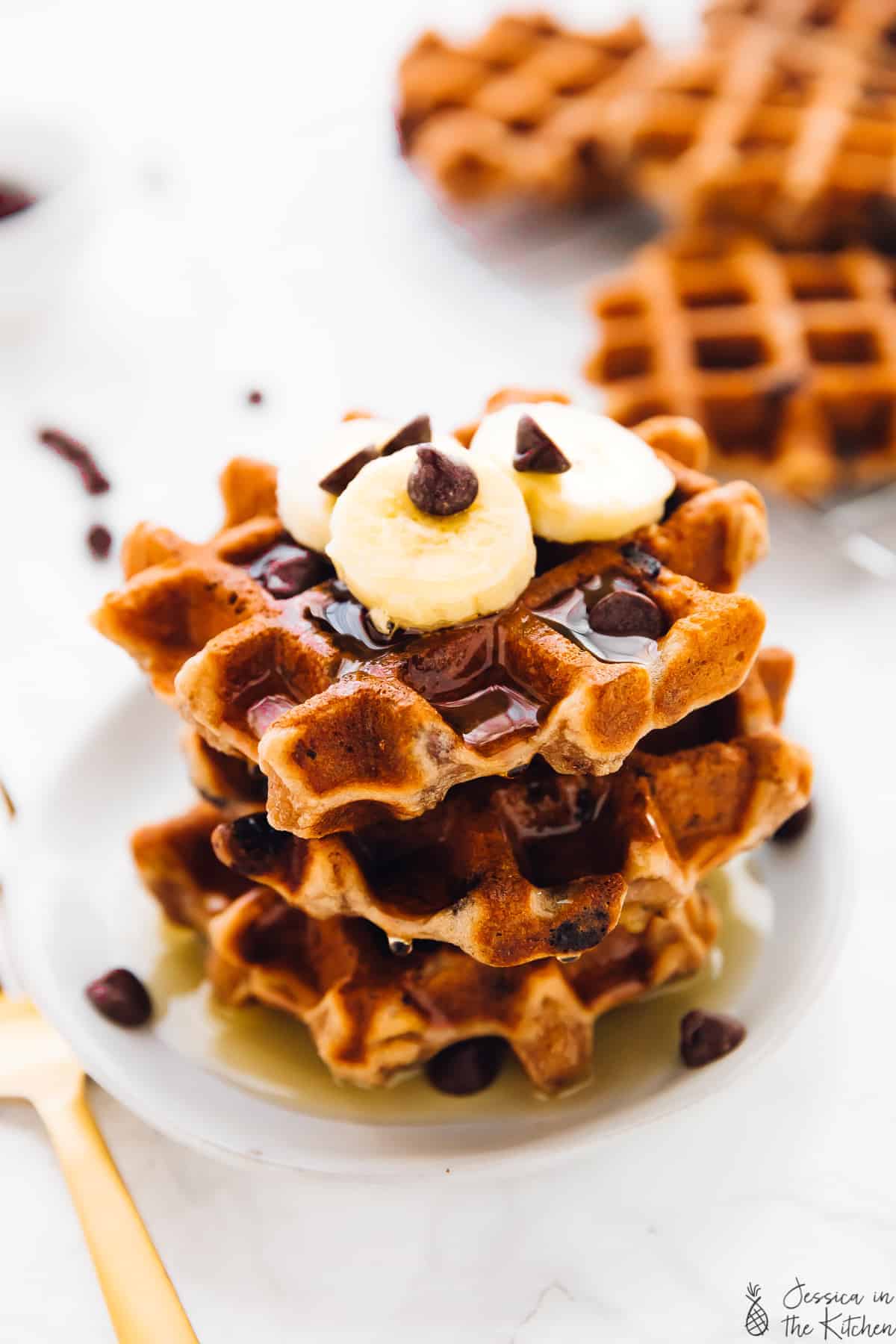 A stack of three banana bread waffles, drizzled in syrup.