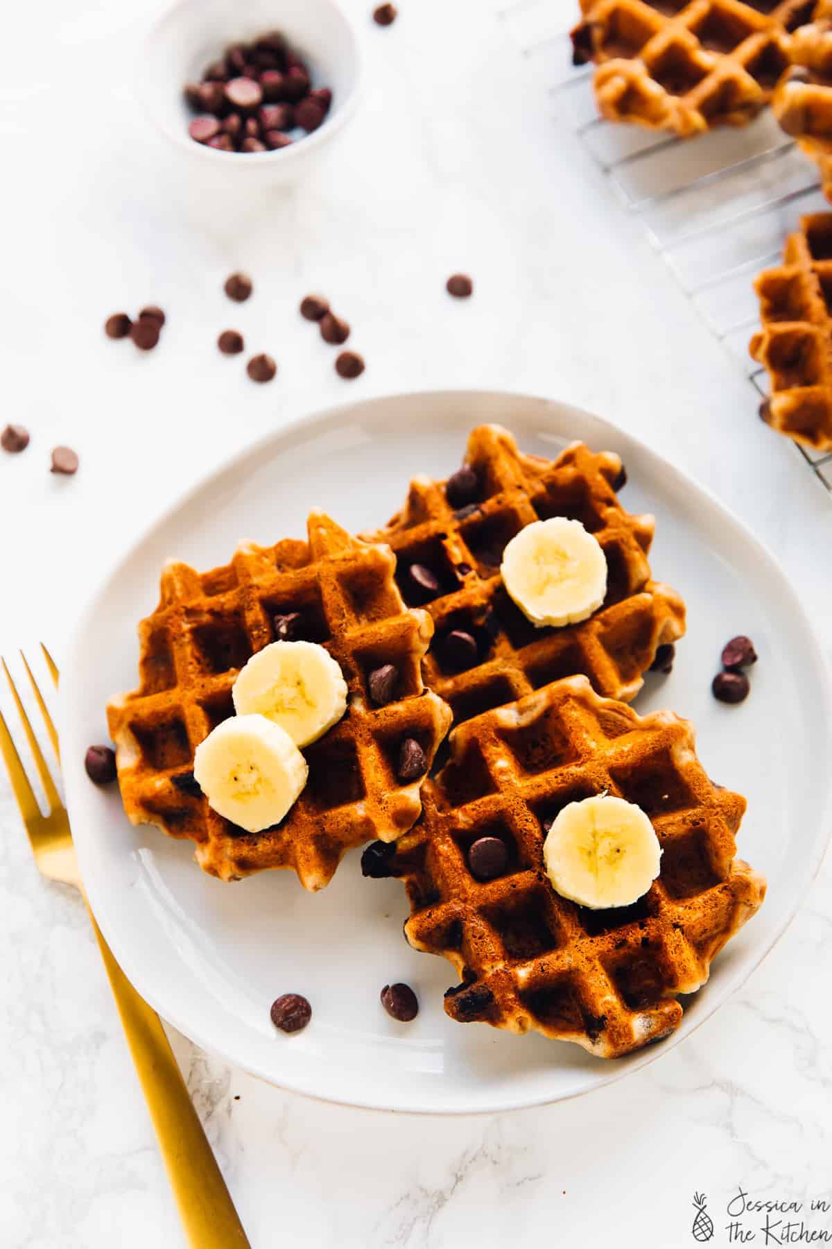 Overhead view of three banana bread waffles on a plate with a gold fork on the side. 