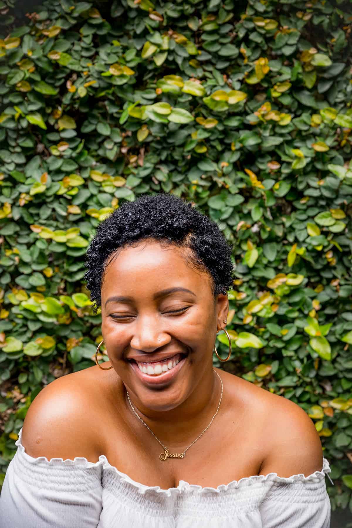 Woman laughing, in front of a bush.