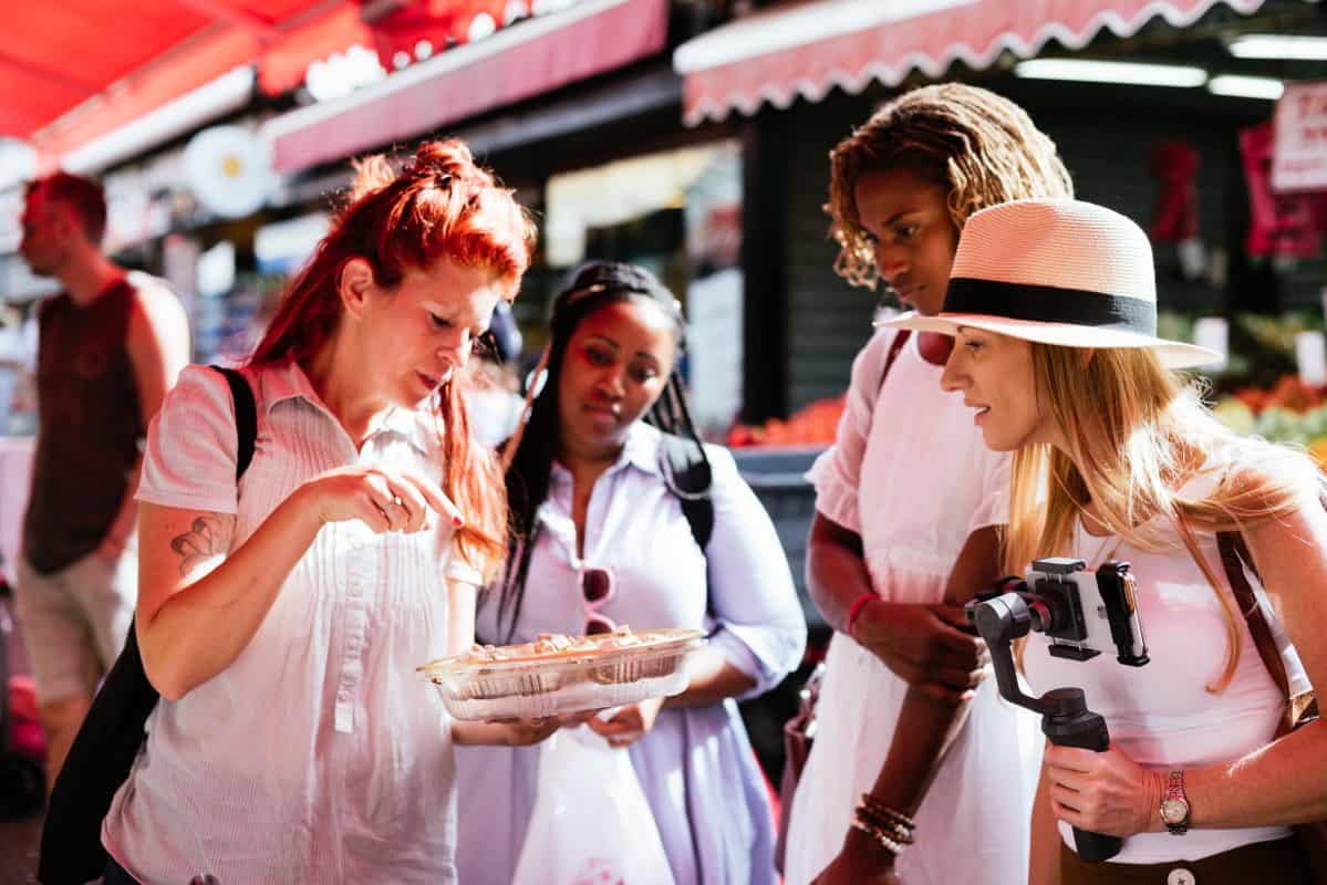 Four women at an open air market, looking at food. 