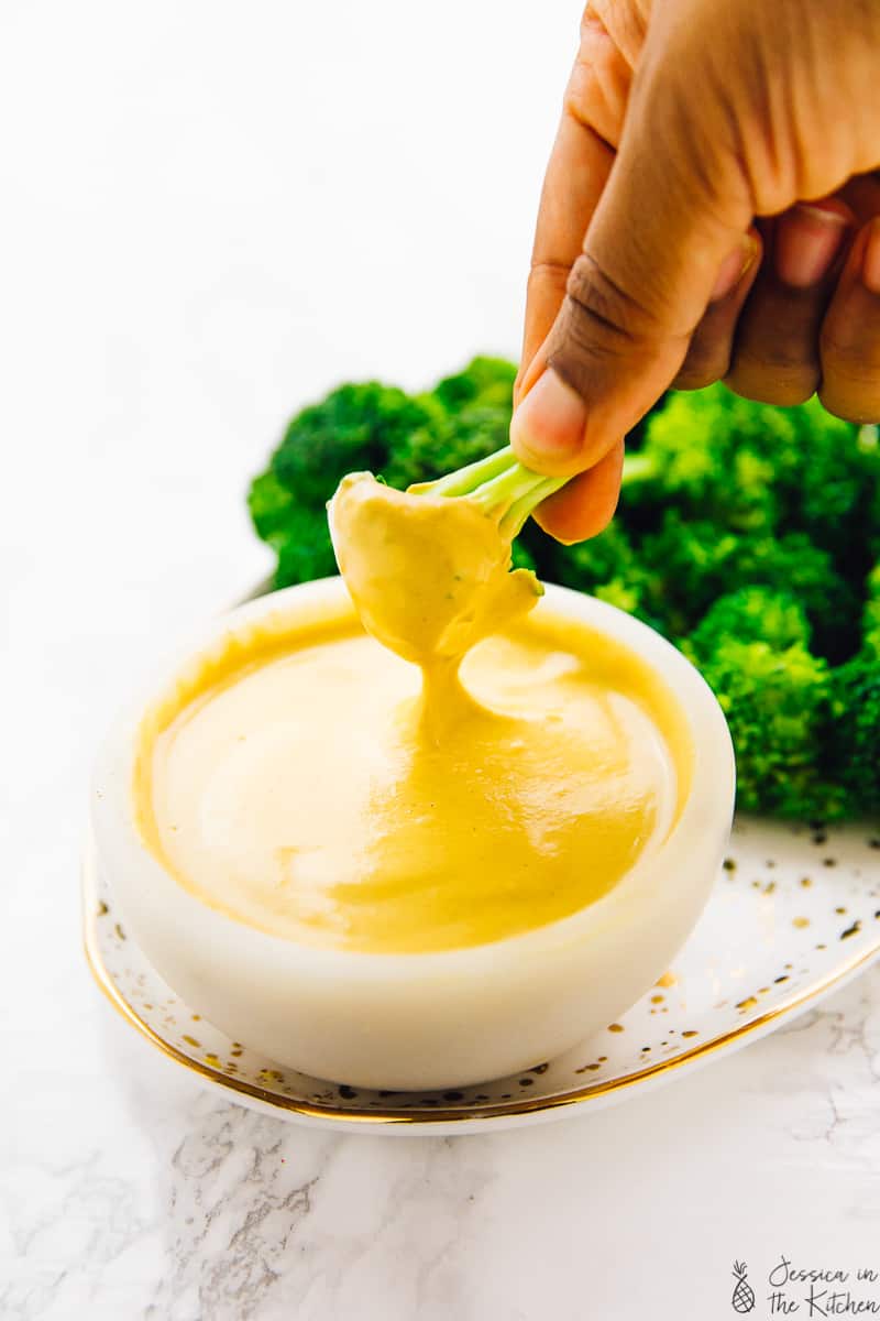 Broccoli being dipped into a bowl of vegan cheese. 