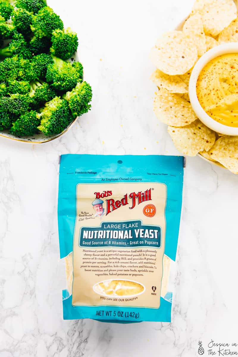 top down view of broccoli in a bowl, vegan cheese in a bowl and a pack of nutritional yeast.