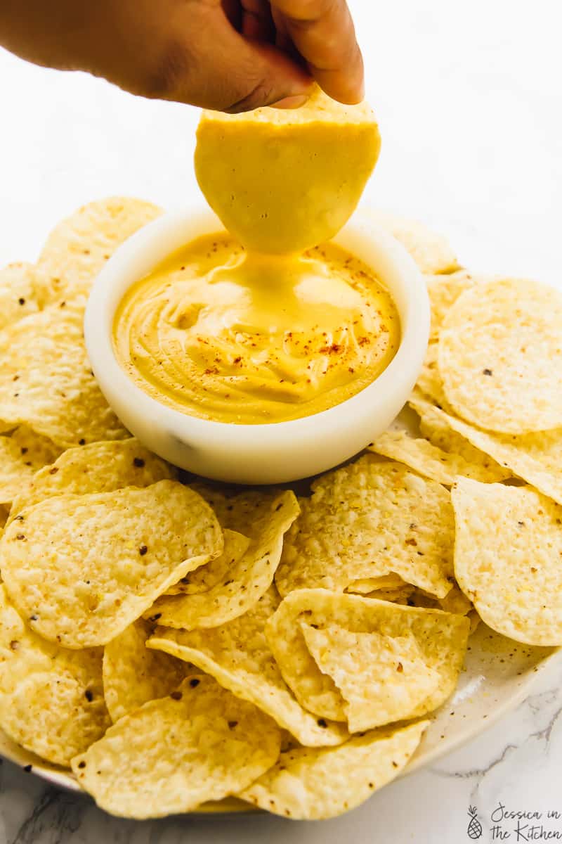 A chip being dipped into some vegan cheese. 