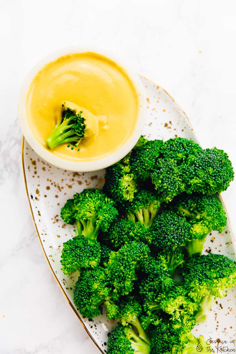 Top down shot of broccoli next to a bowl of vegan cheese. 
