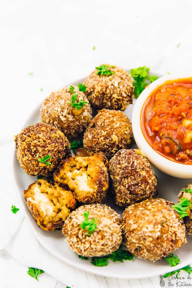 A batch of arancini balls on a plate next to a bowl of dipping sauce. 