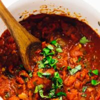 Spicy arrabbiata sauce in a red pot, being stirred.