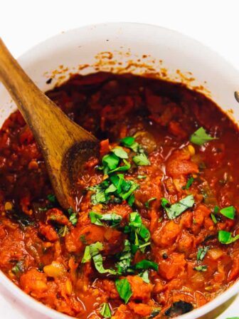 Spicy arrabbiata sauce in a red pot, being stirred.