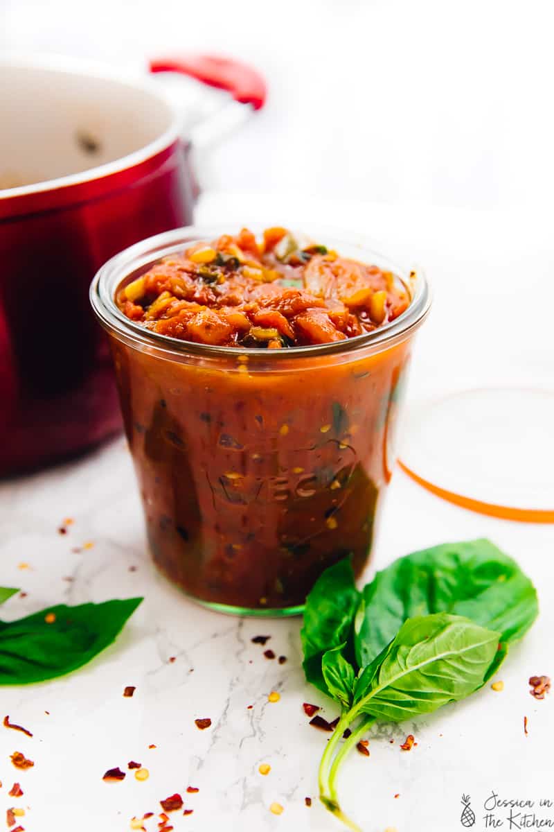 Side shot of spicy arrabbiata sauce in a glass with basil leaves around it. 