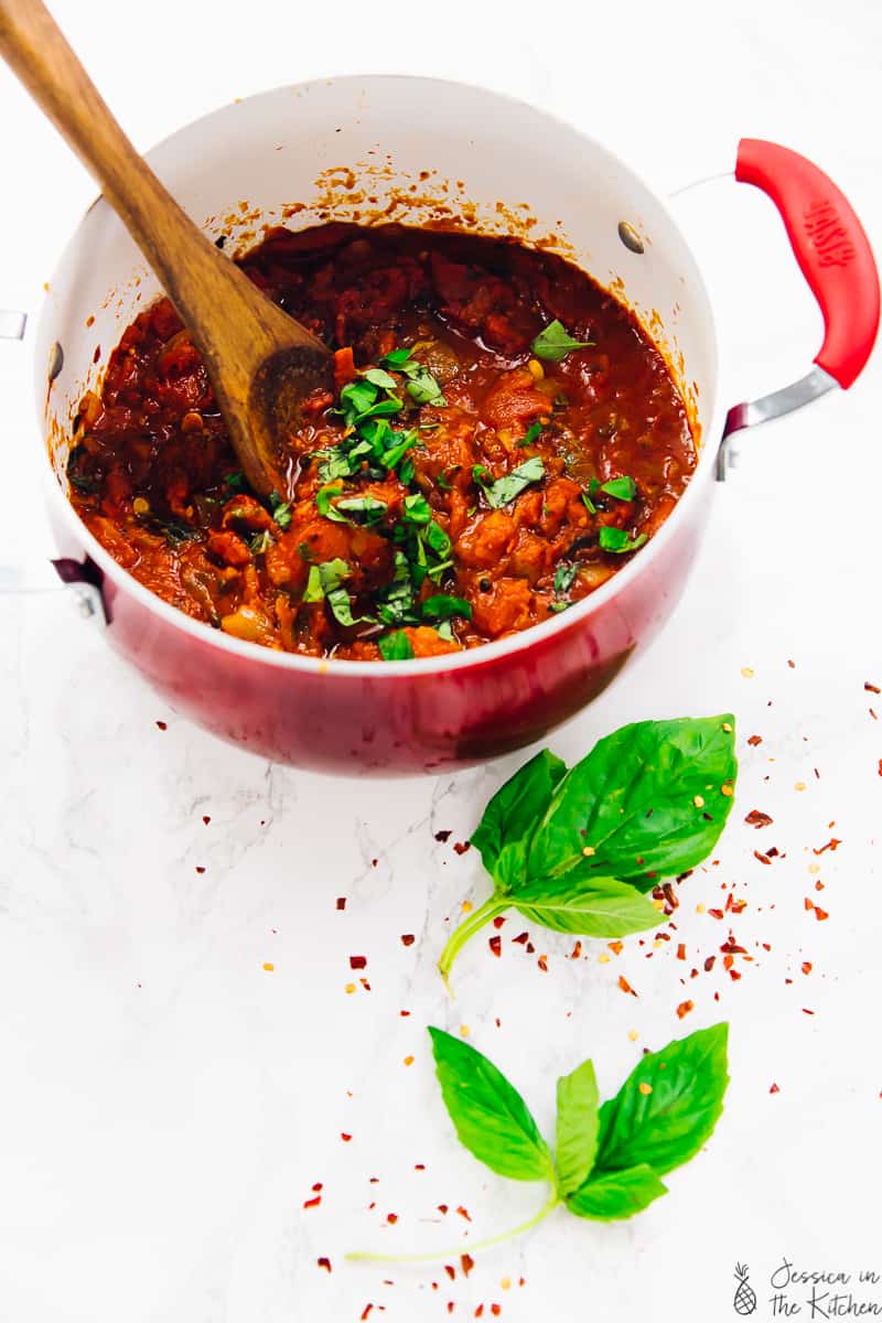 Overhead shot of spicy arrabbiata sauce in a red pot, with basil leaves on the side. 