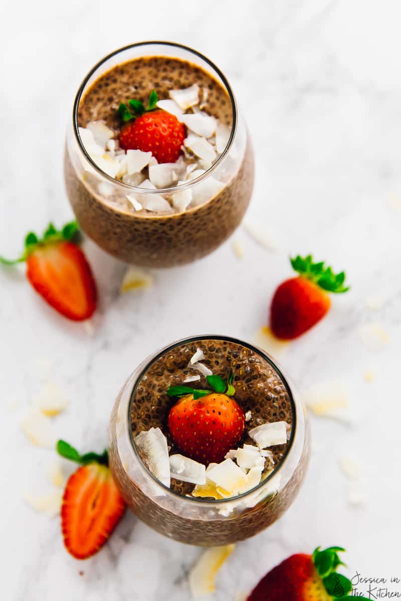 Top down shot of two chia puddings in a glasses, with sliced strawberries on the side. 