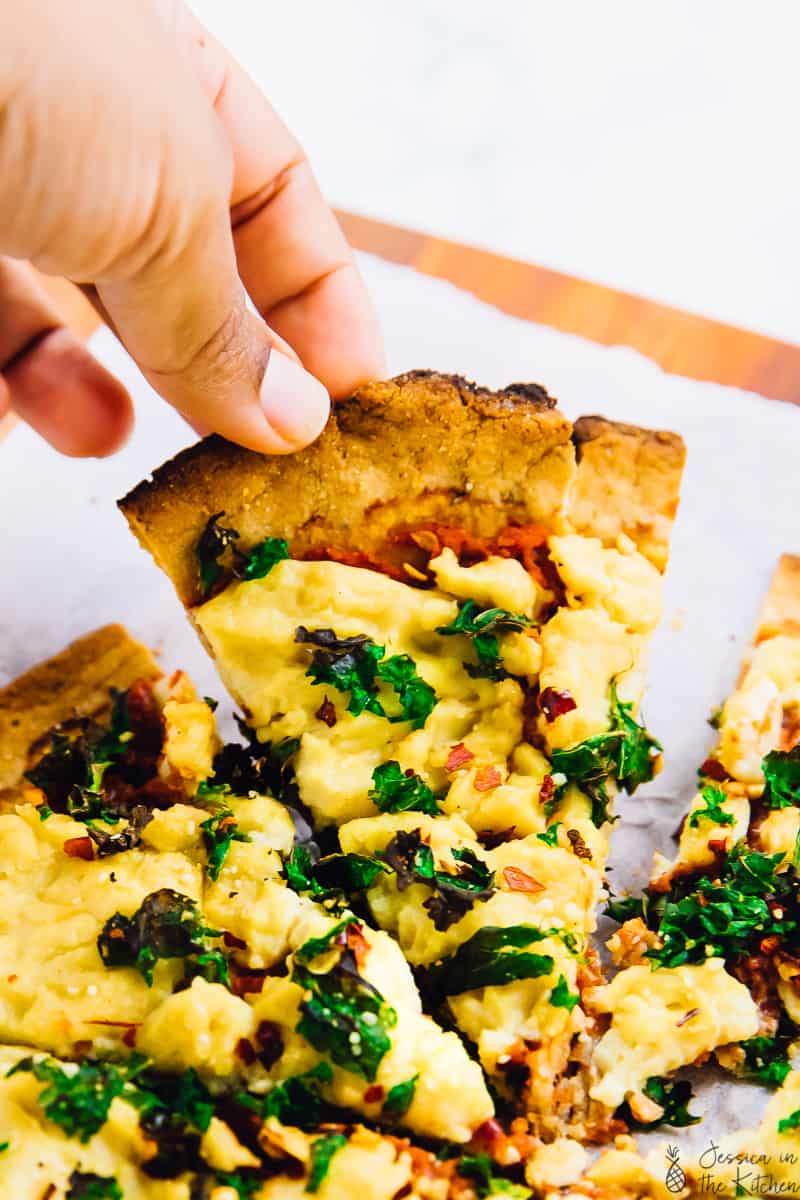 A hand pulling on a slice of vegan almond flour pizza crust.