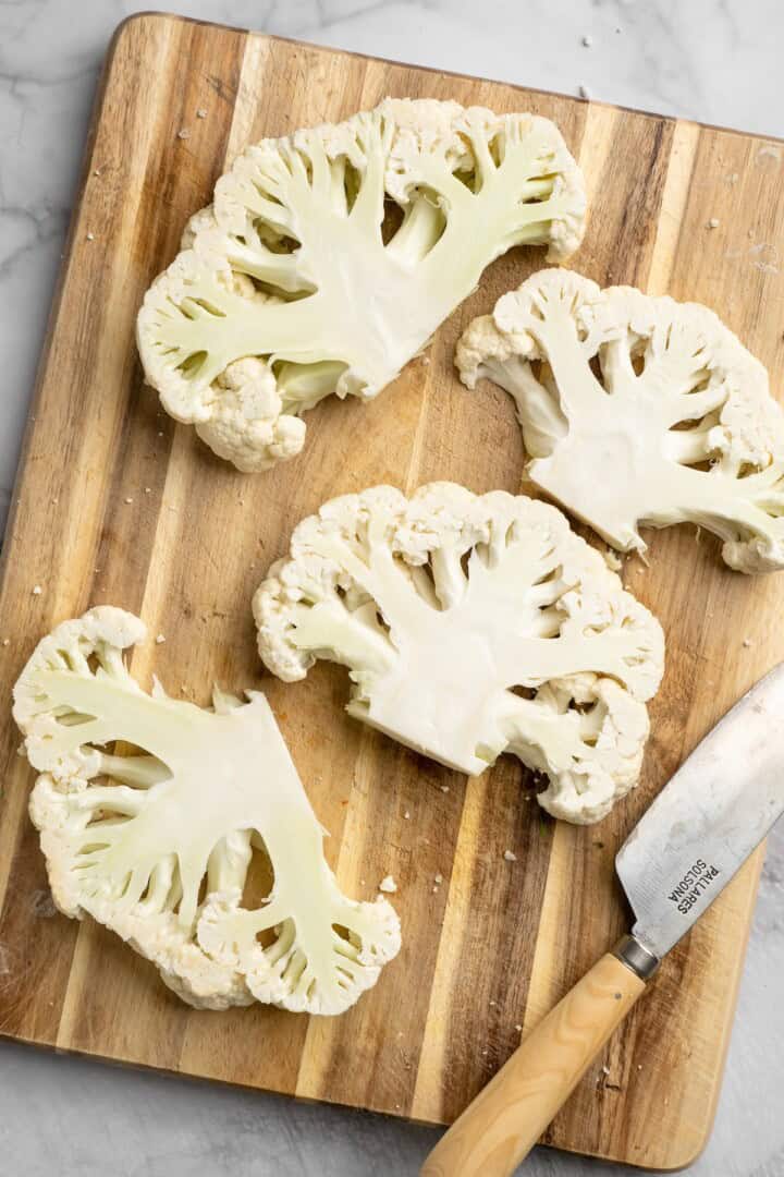 Overhead view of cauliflower steaks on cutting board with knife