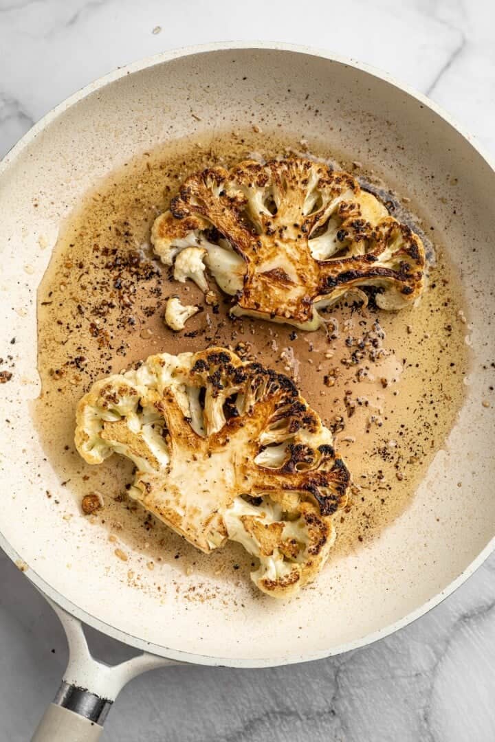 Overhead view of cauliflower steaks being seared in pan