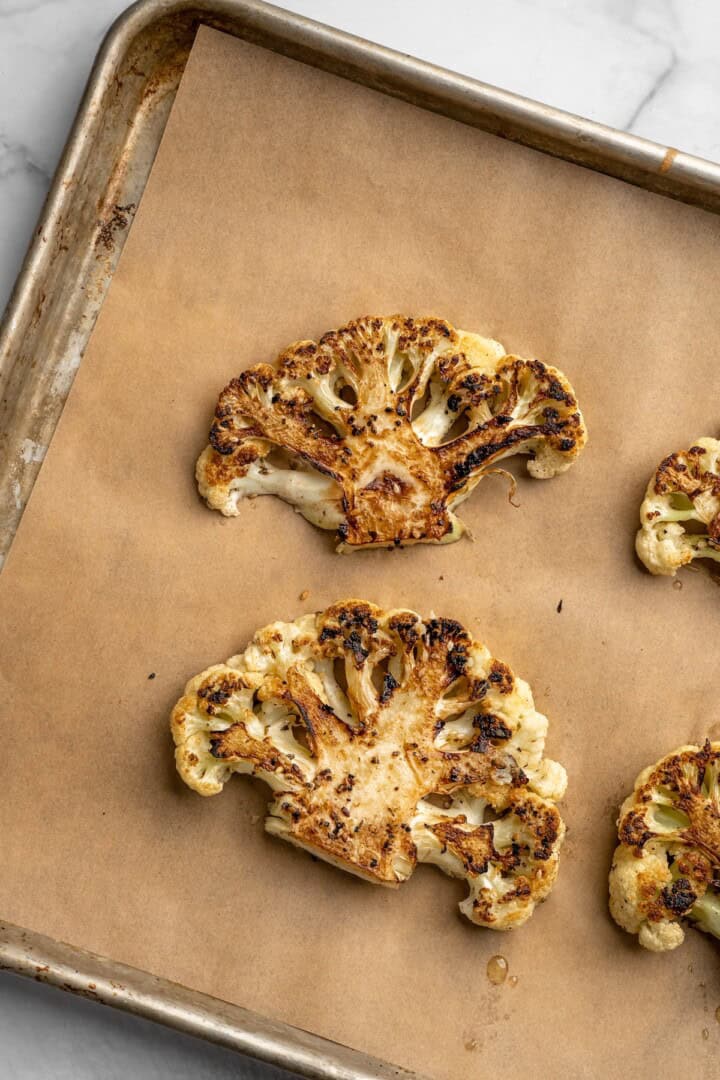 Overhead view of roasted cauliflower steaks on parchment-lined pan