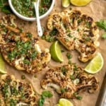 Overhead view of cauliflower steaks on sheet pan with chimichurri in bowl