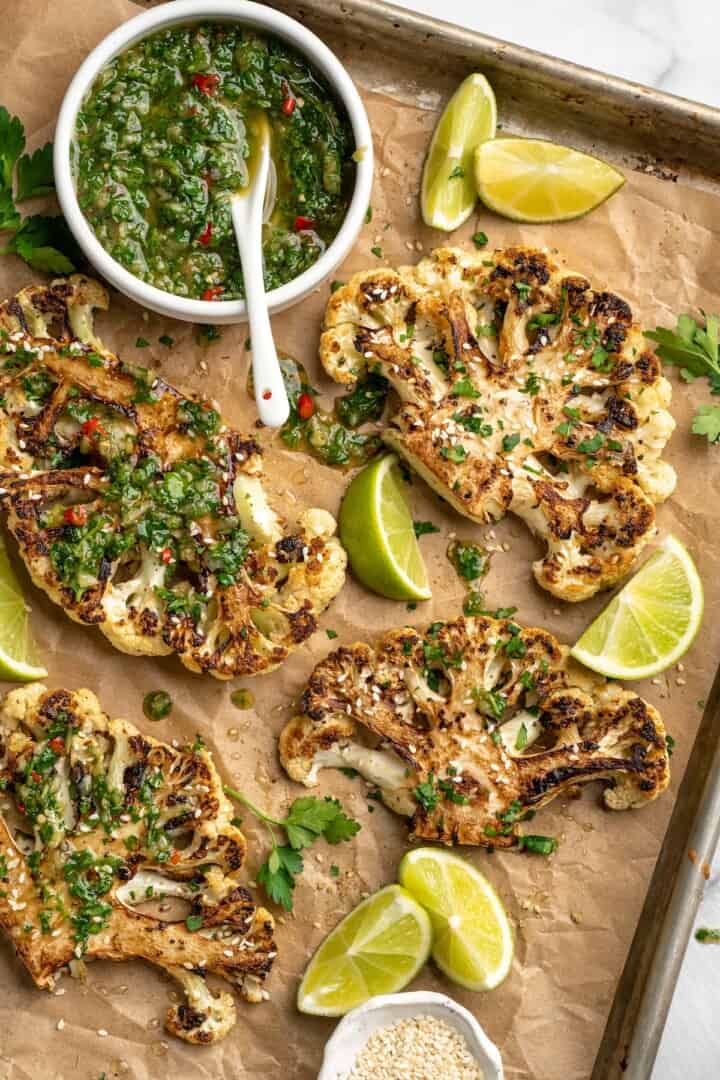 Overhead view of cauliflower steaks on sheet pan with chimichurri in bowl