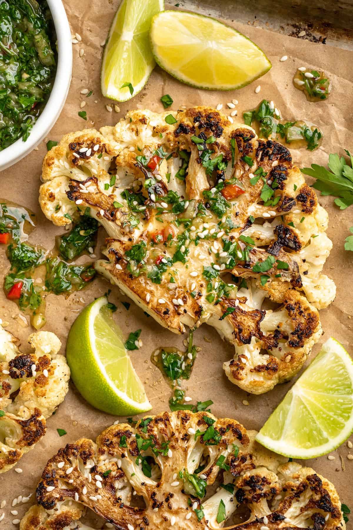 Overhead view of cauliflower steaks on sheet pan drizzled with chimichurri