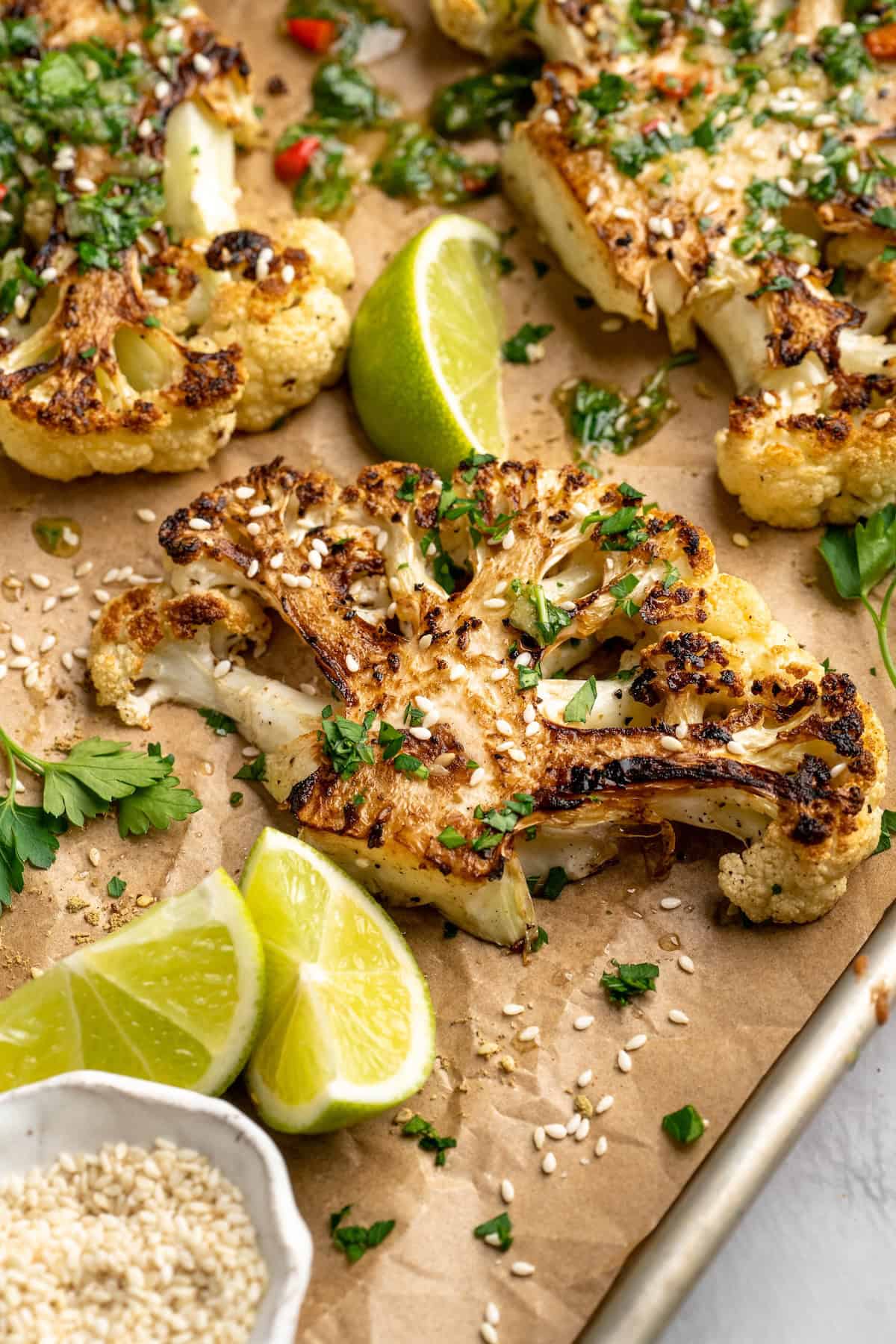 Cauliflower steaks on sheet pan with lime wedges and sesame seeds for garnish