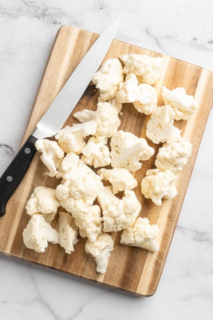 This easy Roasted Cauliflower Hummus gives the classic dip a low-carb makeover! I add roasted garlic too, which makes it extra delicious. Overhead view of cut cauliflower florets on cutting board
