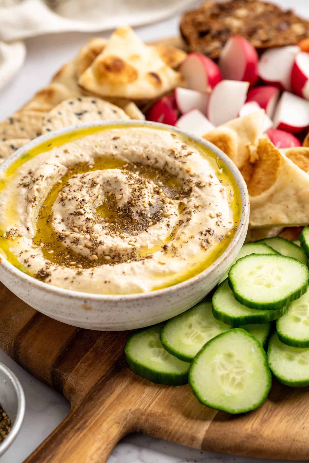 This easy Roasted Cauliflower Hummus gives the classic dip a low-carb makeover! I add roasted garlic too, which makes it extra delicious. Bowl of roasted cauliflower hummus on board with vegetables