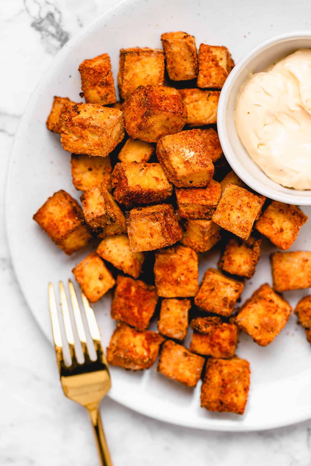 air fryer tofu on a plate with sauce and a gold fork