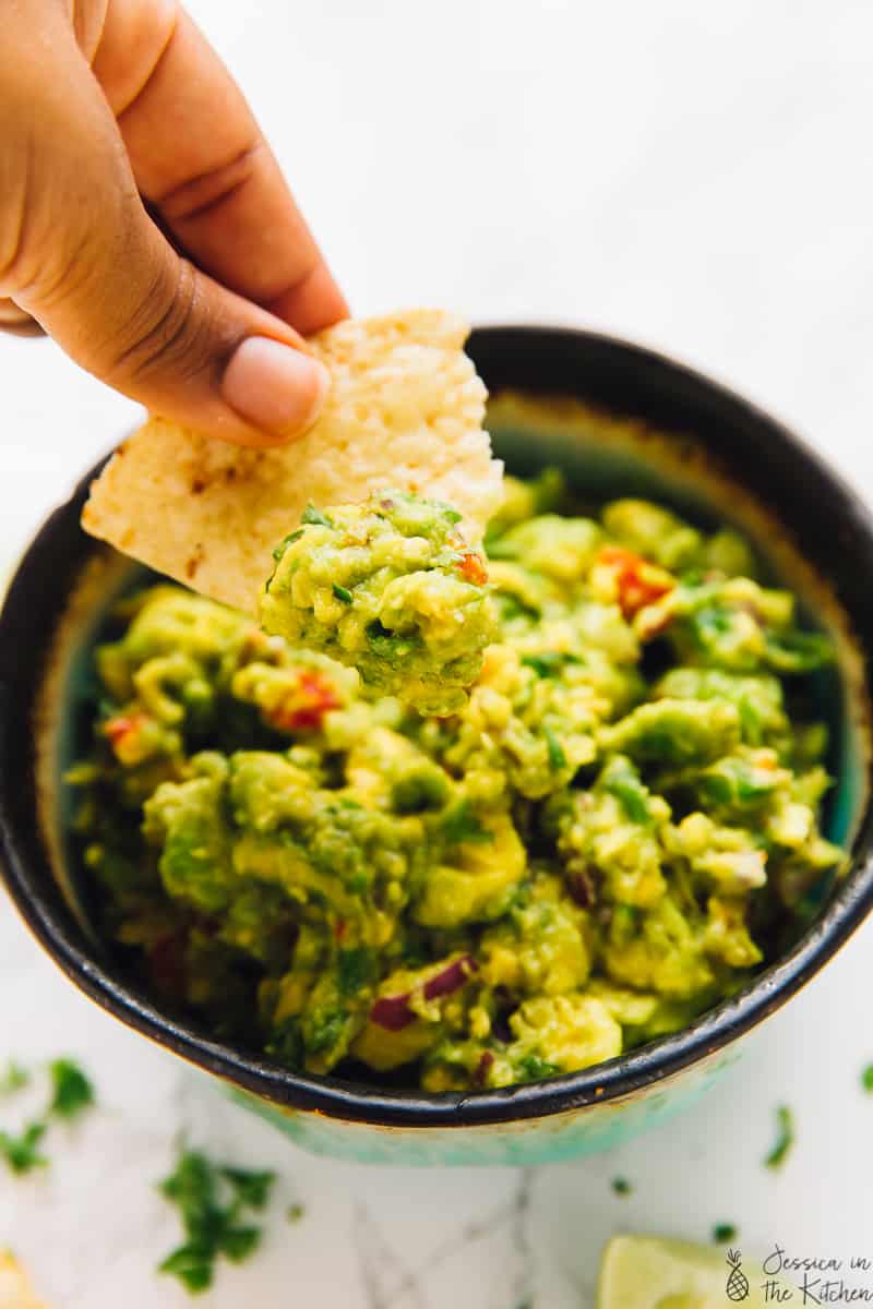 A hand dipping a tortilla chip into a bowl of guacamole.